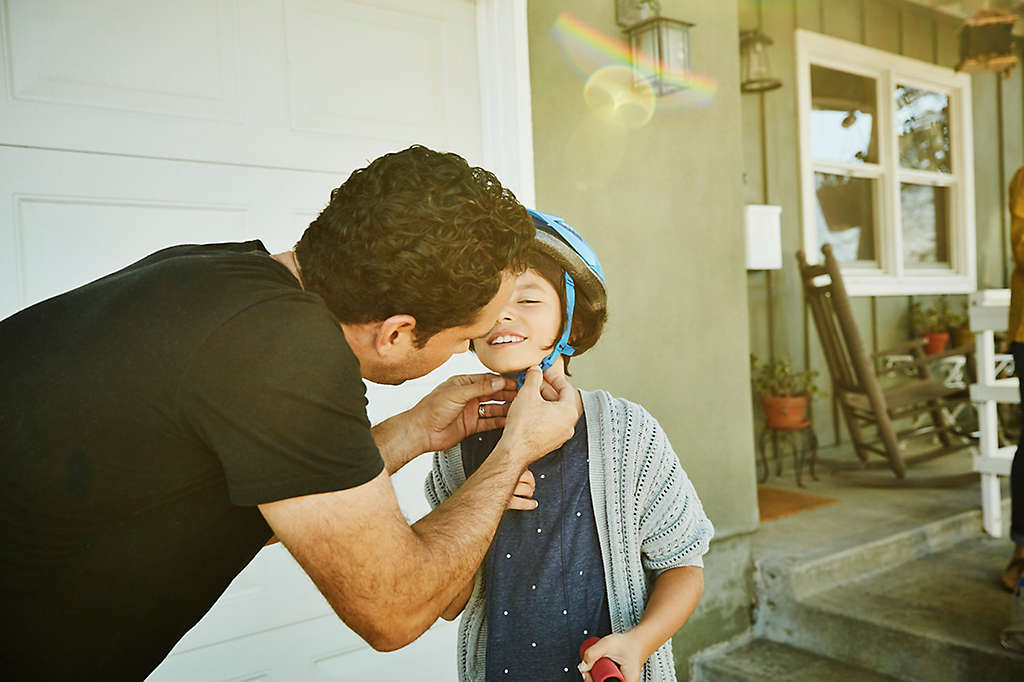 A father puts a helmet on his son before the boy rides his bicycle, because protection is important.