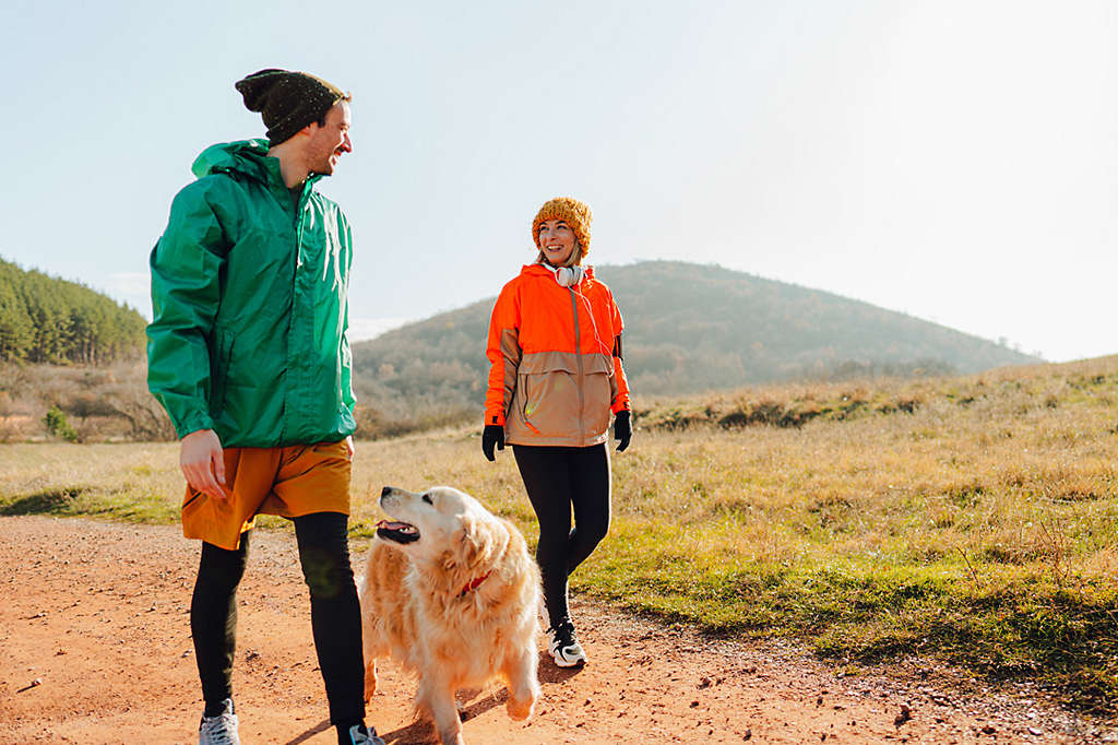 Photo of young couple who enjoy being outdoors, spending sunny winter day out in the woods with their dog