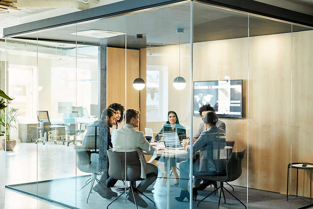 Business colleagues sitting at conference table seen through glass wall. Multi-ethnic coworkers are discussing in board room at office. They are planning strategy.