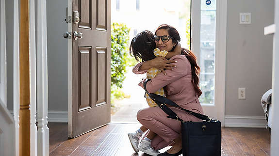 Toddler girl embracing mother in doorway as she gets home from work.
