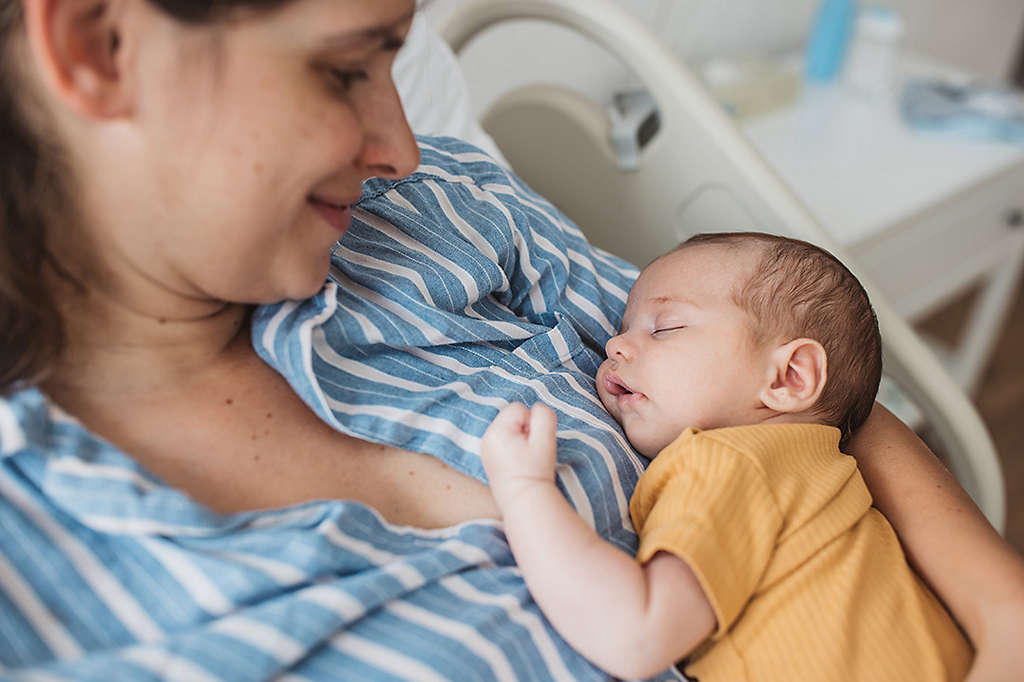 Mother holding new born baby at hospital bed.