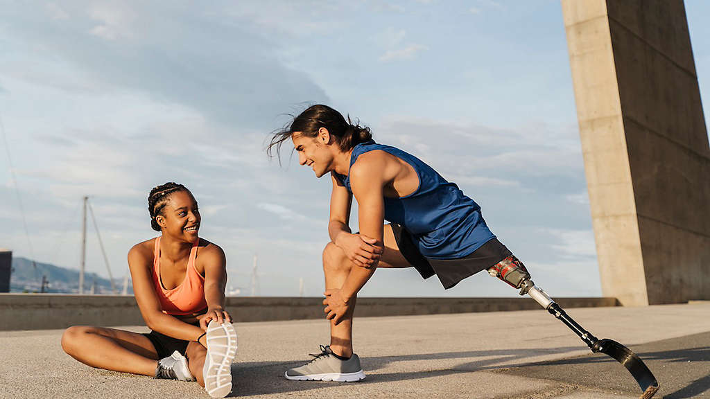Young man with prosthetic leg and his friend stretching after a run