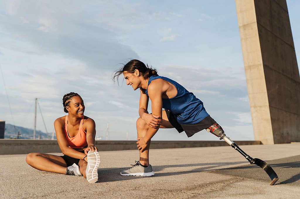 Young man with prosthetic leg and his friend stretching after a run