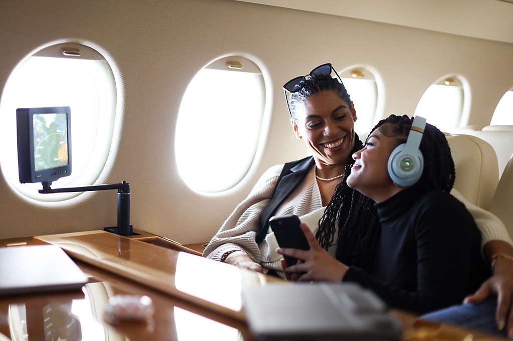 A mother and daughter smile at each other while traveling on a private jet