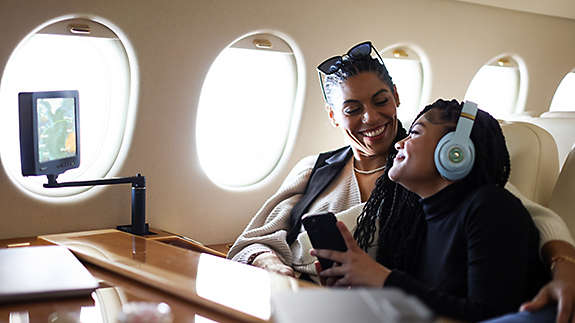 A mother and daughter smile at each other while traveling on a private jet