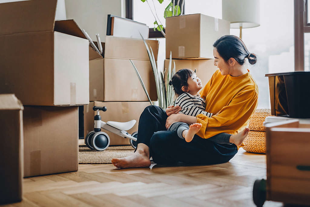 A parent laughing and playing with the child they are carrying on their back.