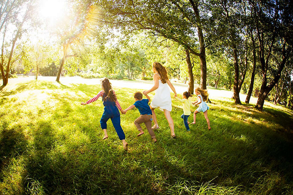 Young parent running with kids through a sunlit park, with everyone holding hands
