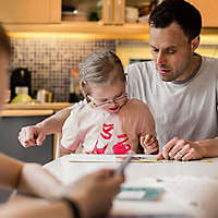 A father reading a book with his daughter at the kitchen table.