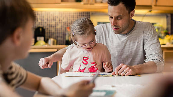 A father reading a book with his daughter at the kitchen table.