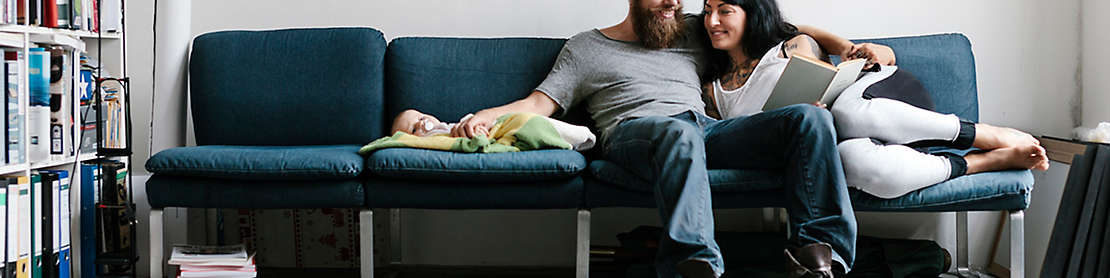 A couple sitting on the couch with their new baby.