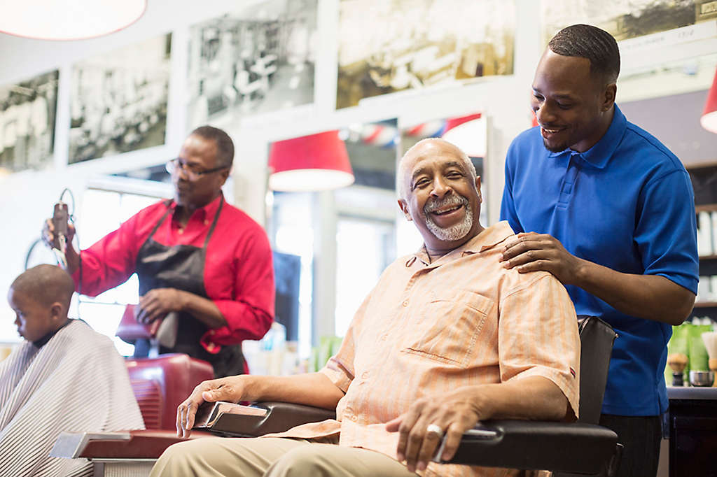 Two men taking care of customers in a barbershop.