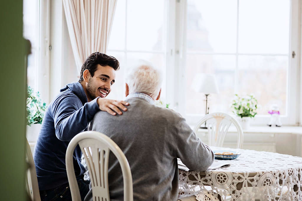 Happy caretaker communicating to senior man in nursing home.