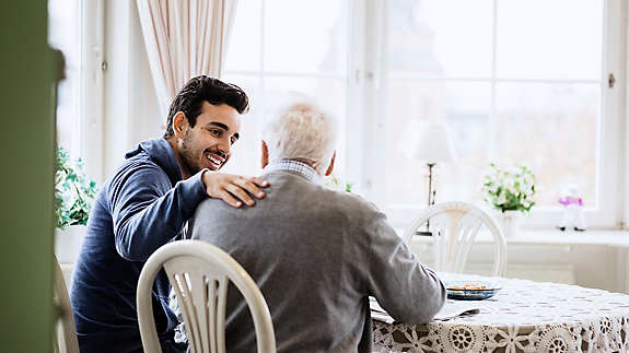 Happy caretaker communicating to senior man in nursing home.