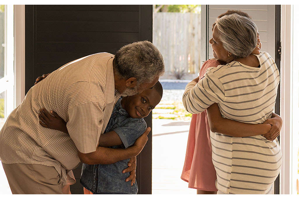 Grandparents hugging their grandchildren by the front door of a house.