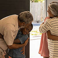 Grandparents hugging their grandchildren by the front door of a house.
