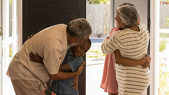 Grandparents hugging their grandchildren by the front door of a house.