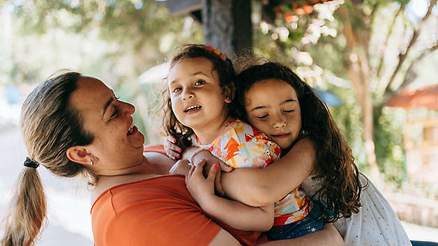 Smiling mother carrying and comforting her two daughters outdoors