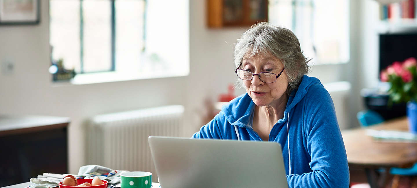 Caucasian woman in her 50s concentrating, peering at screen, working on home finances, planning for retirement