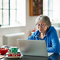 Caucasian woman in her 50s concentrating, peering at screen, working on home finances, planning for retirement