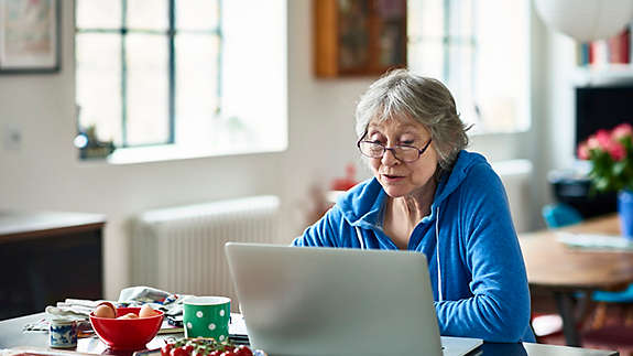 Caucasian woman in her 50s concentrating, peering at screen, working on home finances, planning for retirement