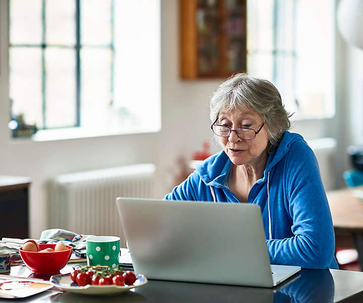 Caucasian woman in her 50s concentrating, peering at screen, working on home finances, planning for retirement