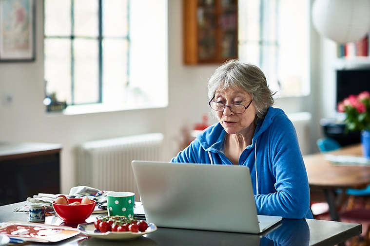 Caucasian woman in her 50s concentrating, peering at screen, working on home finances, planning for retirement