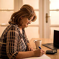 Woman sitting at table with laptop, calculator and cup of coffee.