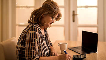 Woman sitting at table with laptop, calculator and cup of coffee.