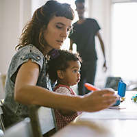 Mom working at the kitchen table with her baby on her lap.