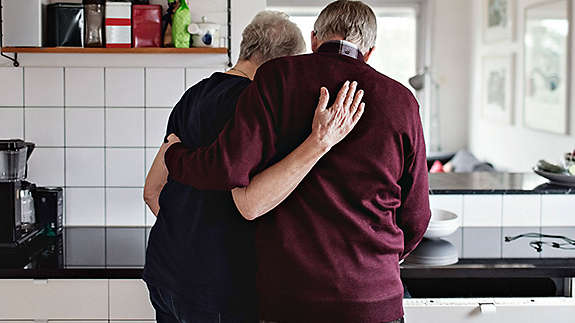Elderly couple in their kitchen hugging each-other.