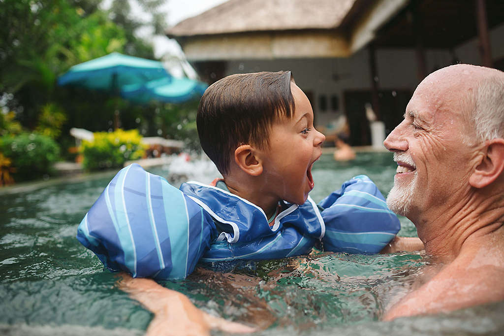 Older gentleman plays with grandchild in the pool