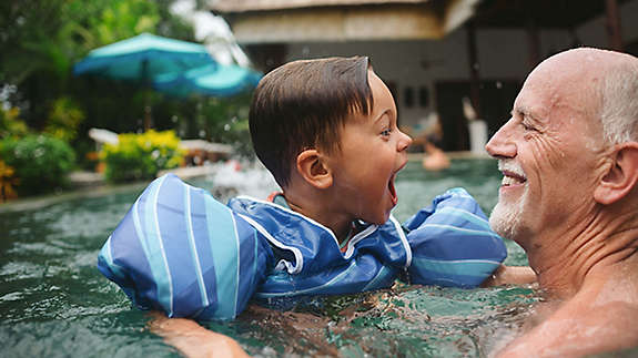 Older gentleman plays with grandchild in the pool