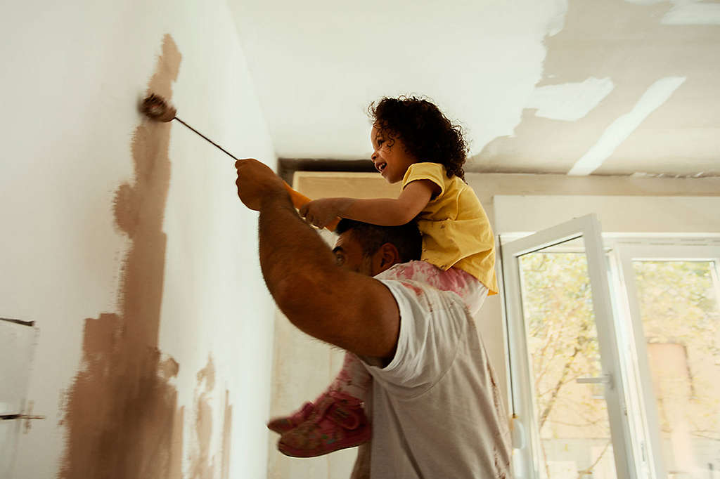 Father painting a room with his young daughter on his shoulders