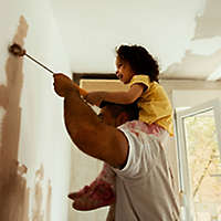 Father painting a room with his young daughter on his shoulders