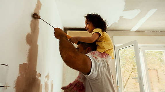 Father painting a room with his young daughter on his shoulders