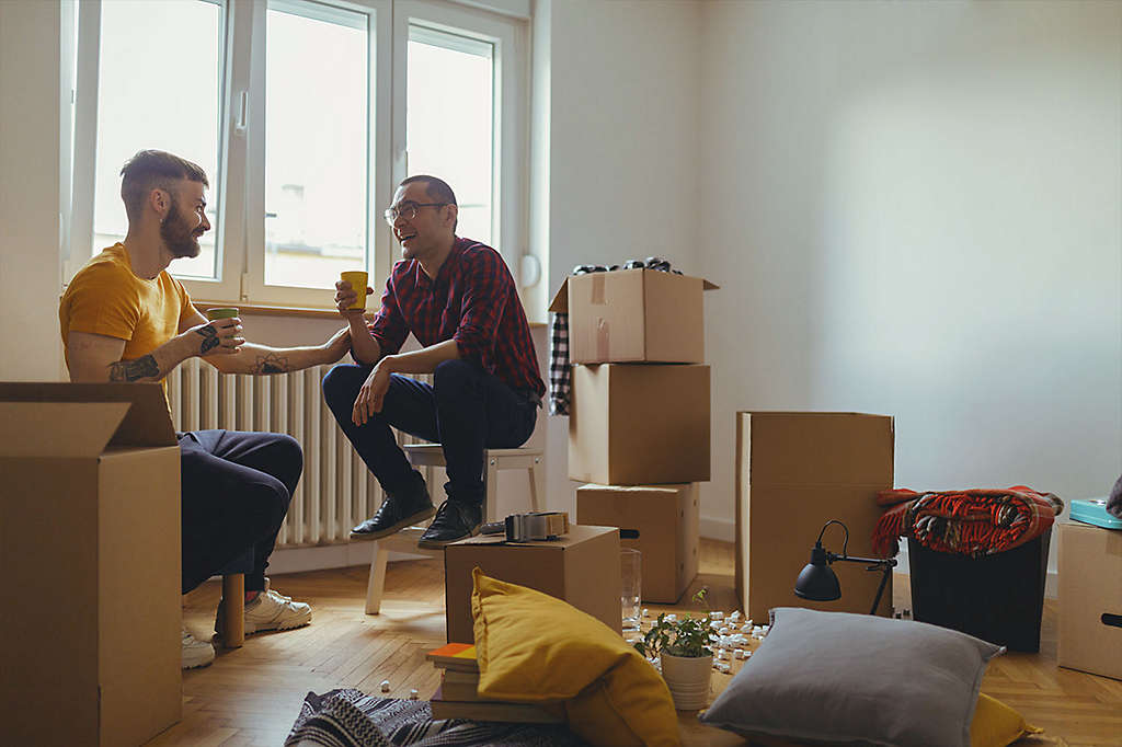 2 male friends sit in room of unpacked boxes