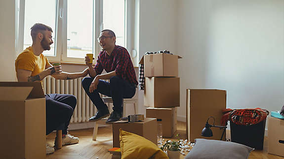 2 male friends sit in room of unpacked boxes