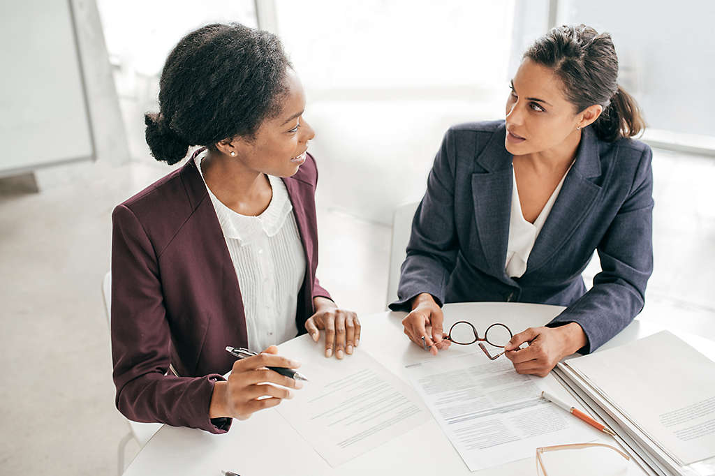 Two women sitting at a table talking and filling out paperwork.