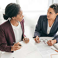 Two women sitting at a table talking and filling out paperwork.