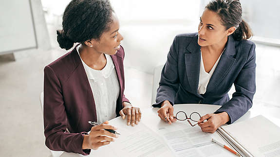 Two women sitting at a table talking and filling out paperwork.