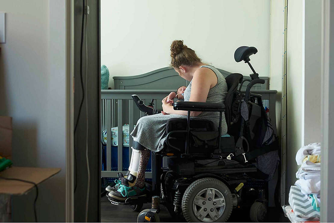 A woman in a wheelchair tends to her baby in a home nursery. 