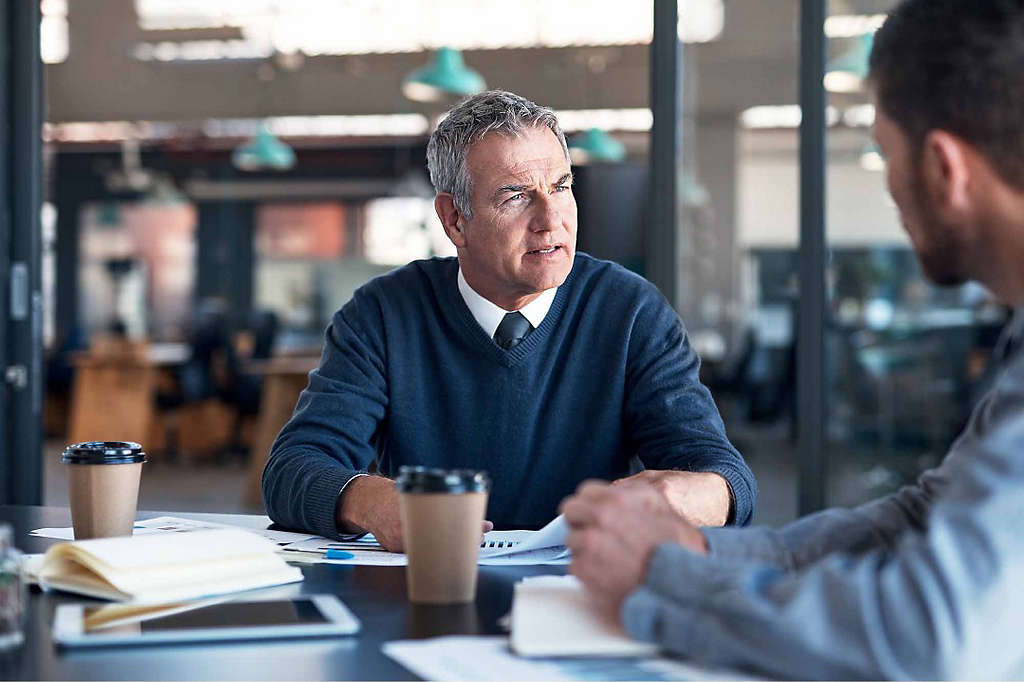 A business owner discusses succession planning with his partner at a boardroom table.