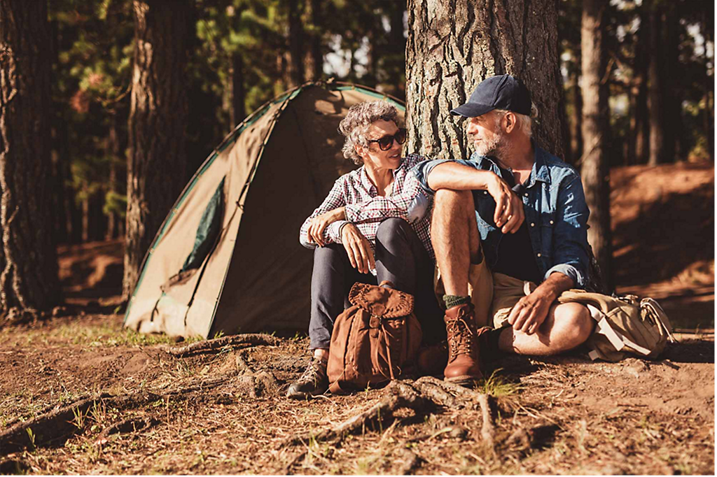 A couple enjoying their retirement, sitting in the sun in the forest while camping