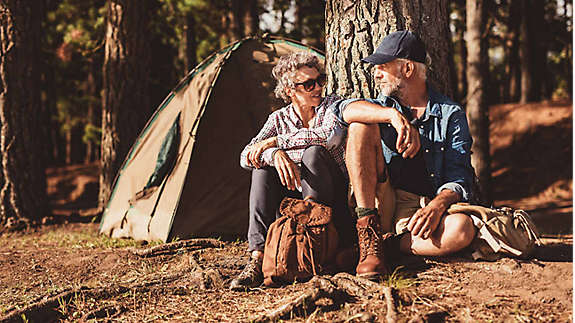 A couple enjoying their retirement, sitting in the sun in the forest while camping