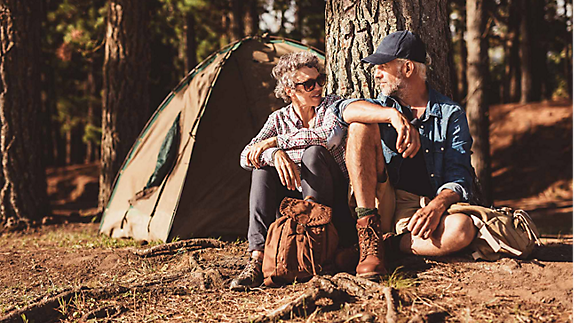 A couple enjoying their retirement, sitting in the sun in the forest while camping