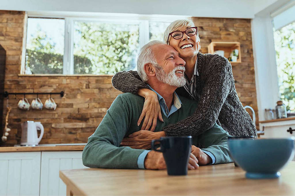 A newly retired couple embracing happily in their kitchen, secure in their investments.