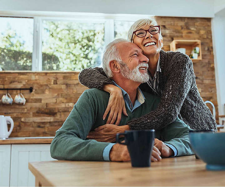 A newly retired couple embracing happily in their kitchen, secure in their investments. 