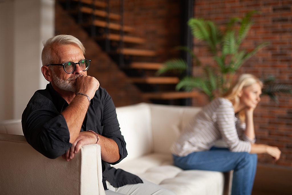 A couple sitting on opposite ends of the couch looking frustrated