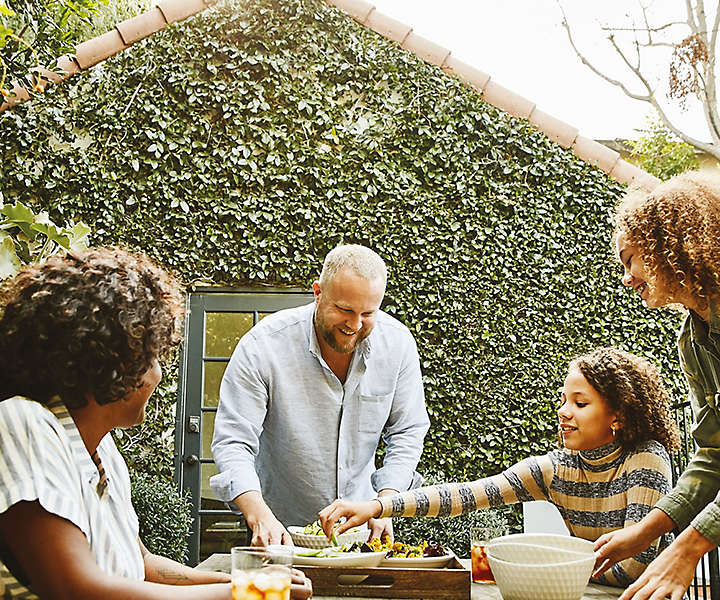 Family in backyard at picnic table eating hors d'oeuvres and drinking iced tea