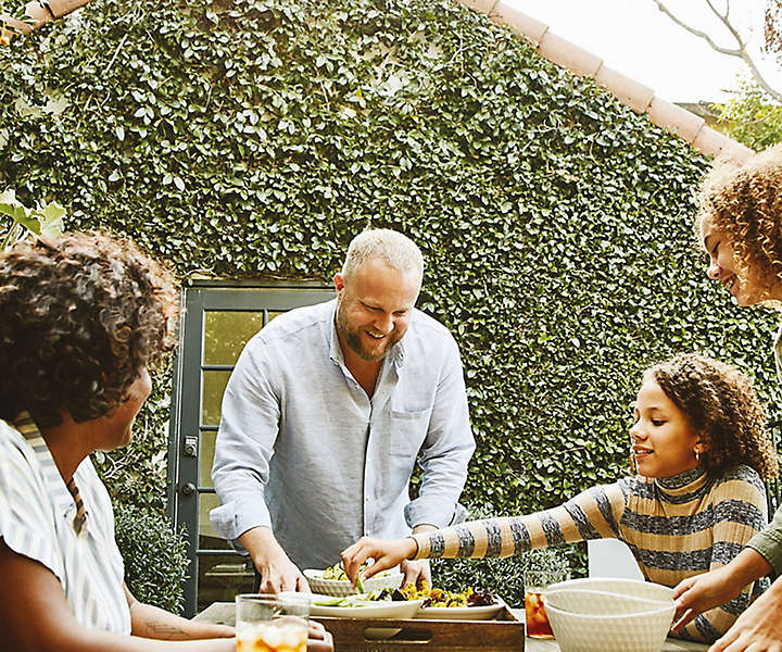 Family in backyard at picnic table eating hors d'oeuvres and drinking iced tea